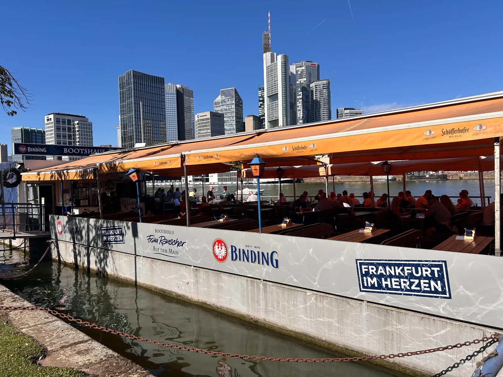 Open-air tables at Bootshaus Frau Rauscher with Frankfurt's skyline behind
