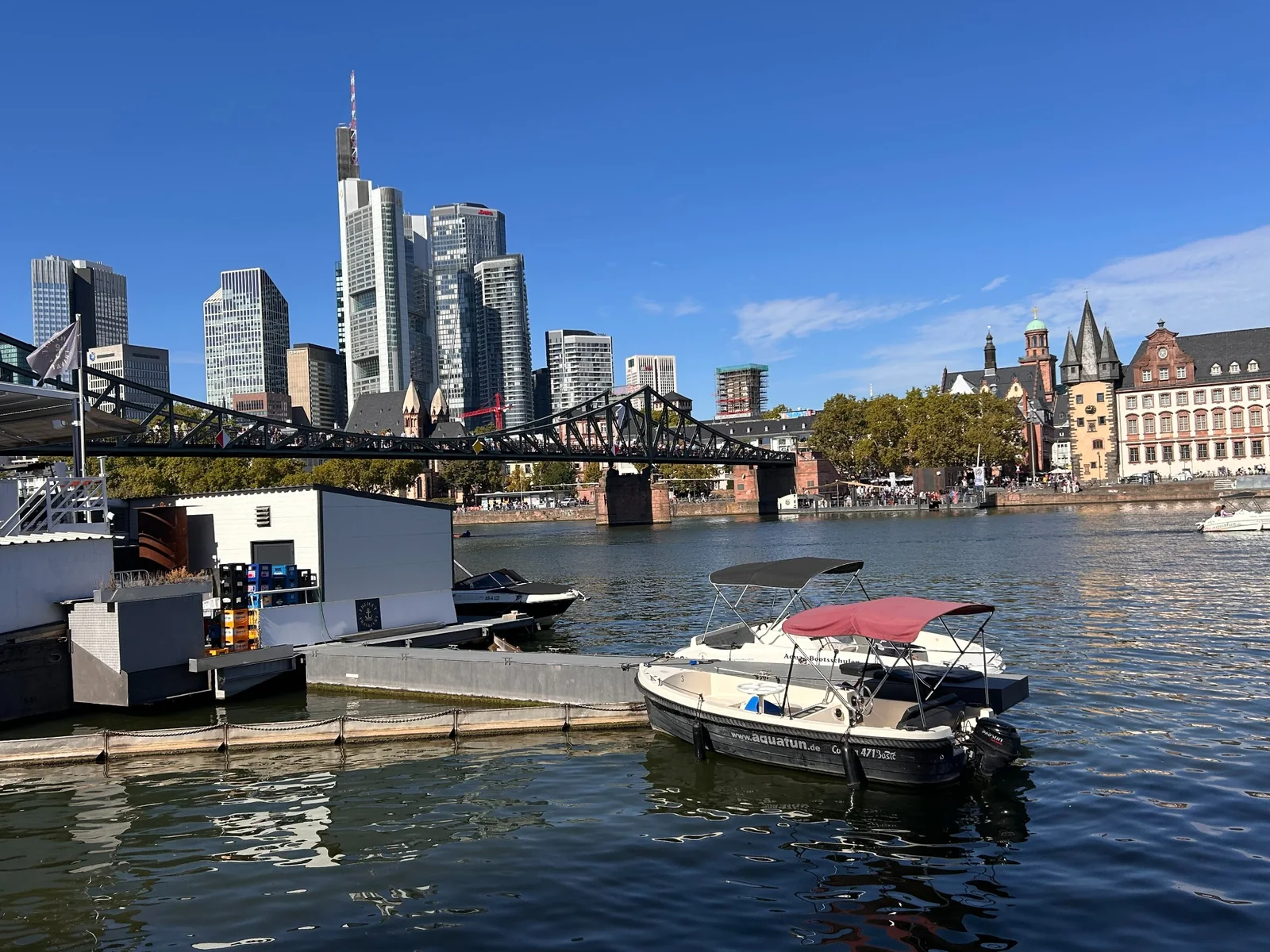Electric rental boats moored beside Eiserner Steg with Frankfurt skyline behind