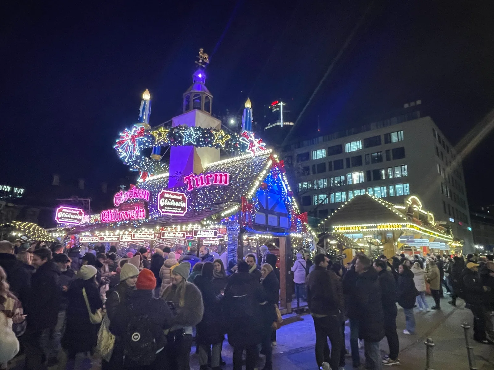 Glühwein stall lit with colourful Christmas decorations on a busy market evening in Frankfurt