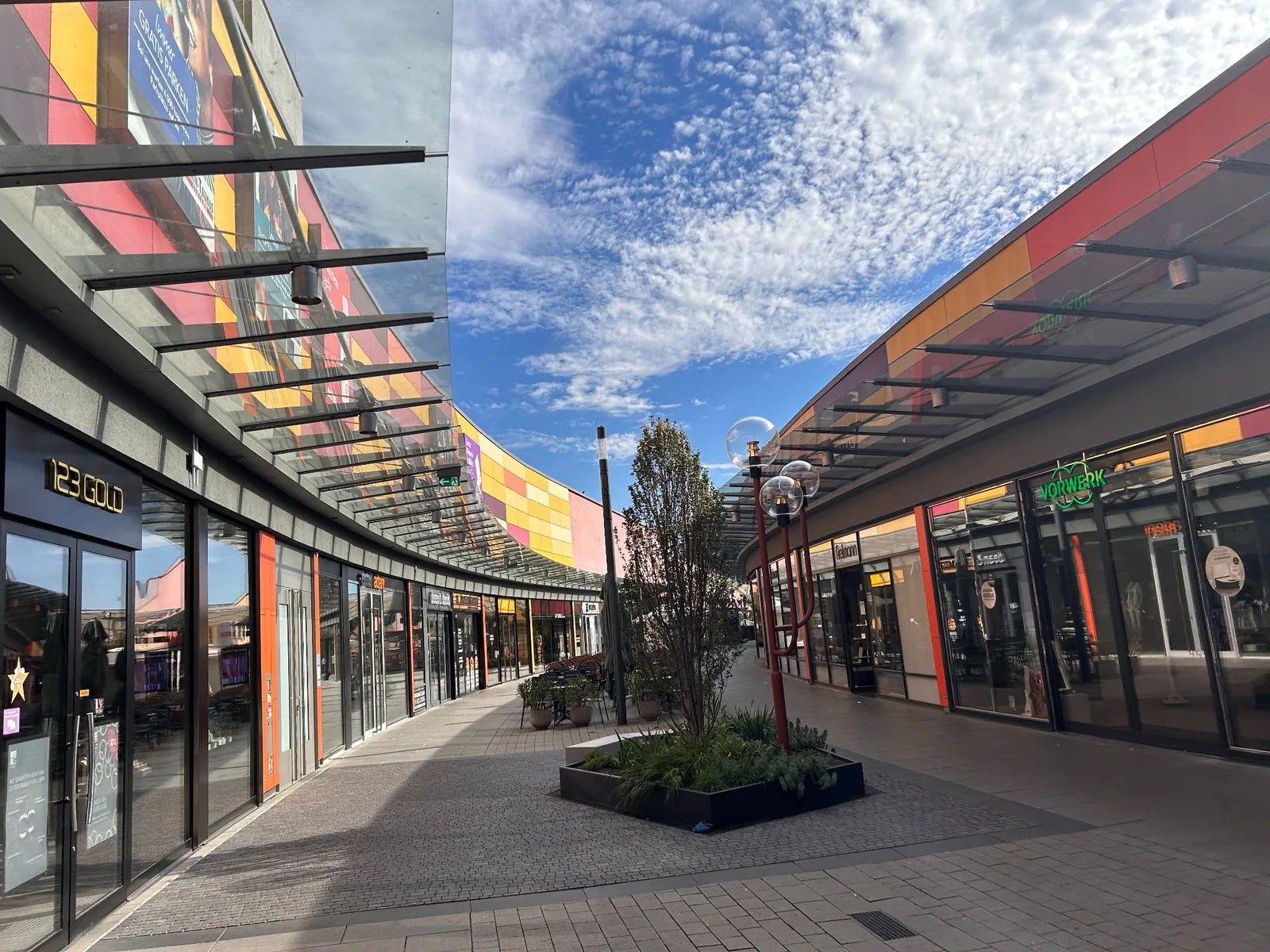 Open-air shopping walkway at Main-Taunus-Zentrum with colourful façades and planting